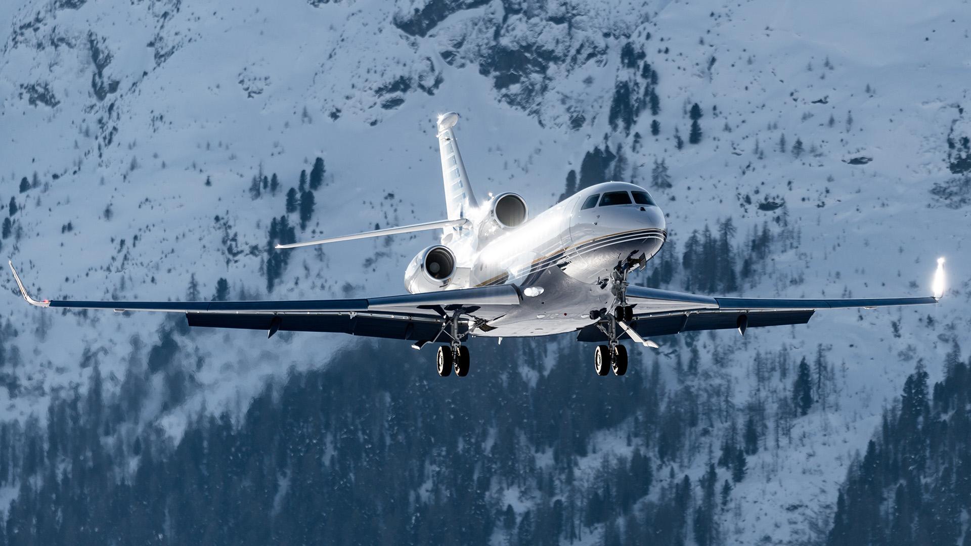 一架三引擎的私人飞机放下了轮子，身后是一片白雪覆盖的山林.